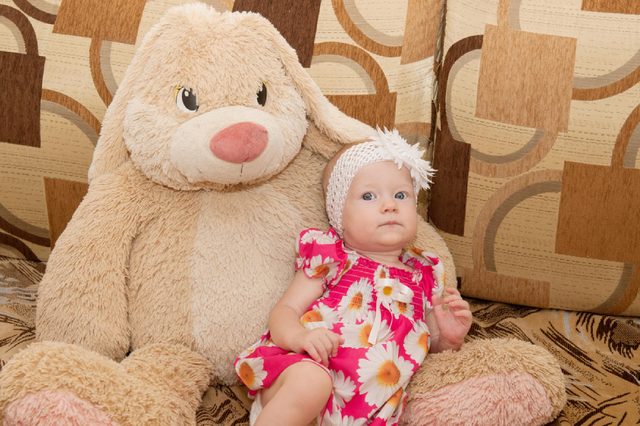 Beautiful expressive adorable happy cute laughing smiling baby infant face. Newborn child relaxing in bed. Nursery for young children. Family morning at home. funny child in a fashionable red dress