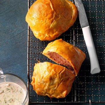 Golden pastries rest on a cooling rack beside a knife, with creamy dipping sauce in a glass bowl on a dark tabletop.