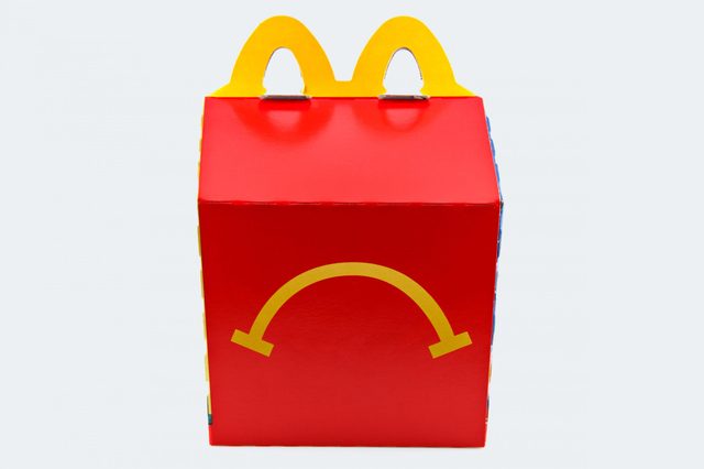 A red cardboard box displays a yellow smile graphic, featuring two yellow handles resembling arches on a plain background.