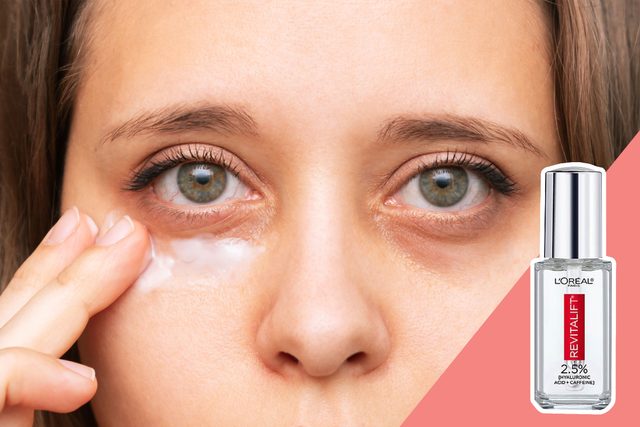 Fingers apply cream under eyes; close-up view. Adjacent is a L'OrÃ©al Revitalift product bottle on a pink background.