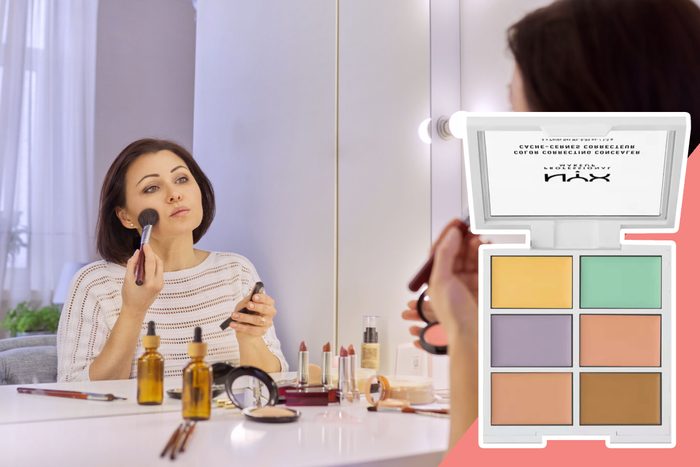 Person applies makeup with a brush at a vanity, surrounded by cosmetics. Inset shows a NYX color-correcting concealer palette.