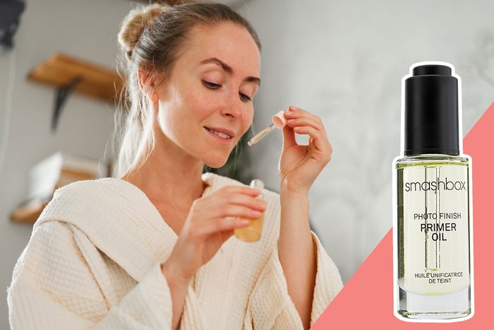 Woman applies primer oil with a dropper, wearing a bathrobe in a bathroom. Text: 