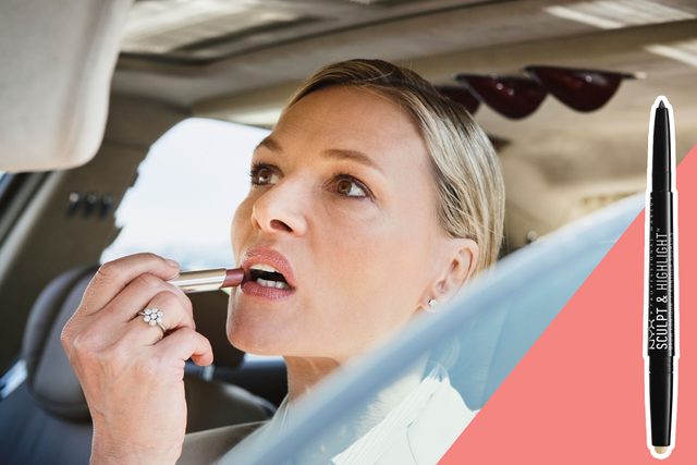 Woman applies lipstick while seated in a car, looking in the mirror. Next to her, a vertical 
