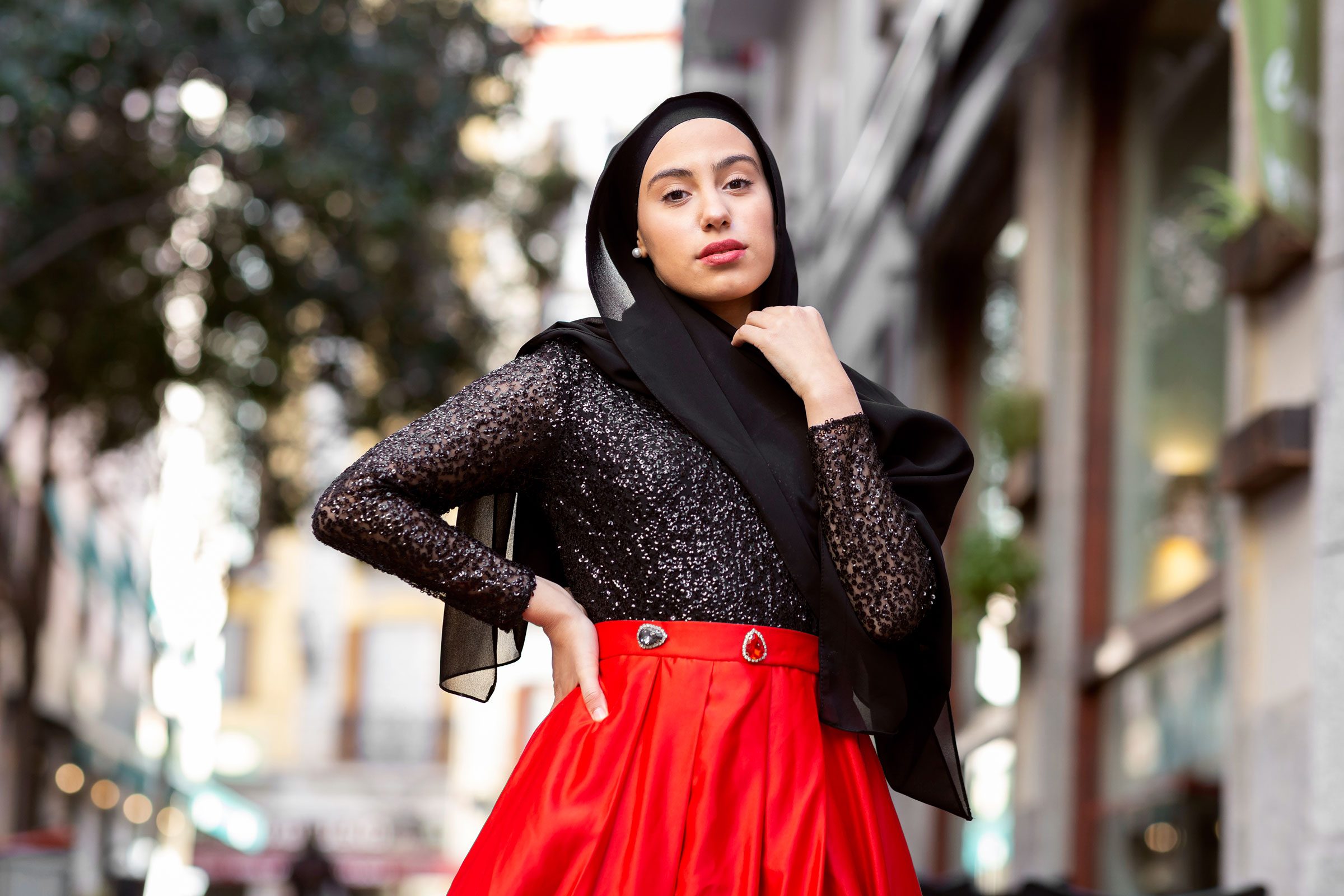 Portrait of young woman wearing black hijab posing outdoors with hand on hip