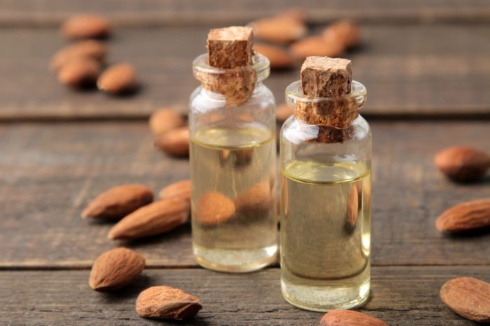 natural almond oil in a glass bottle and fresh almond nuts close-up on a brown wooden table.