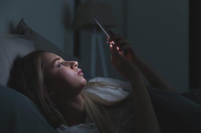 Closeup portrait of young sleepy exhausted woman lying in bed using smartphone, can not sleep/ Insomnia, nomophobia, sleep disorder concept/ Dependency on a cell phone/ Internet addiction
