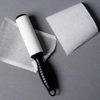 Lint roller lying on gray surface with detached sticky sheets nearby.