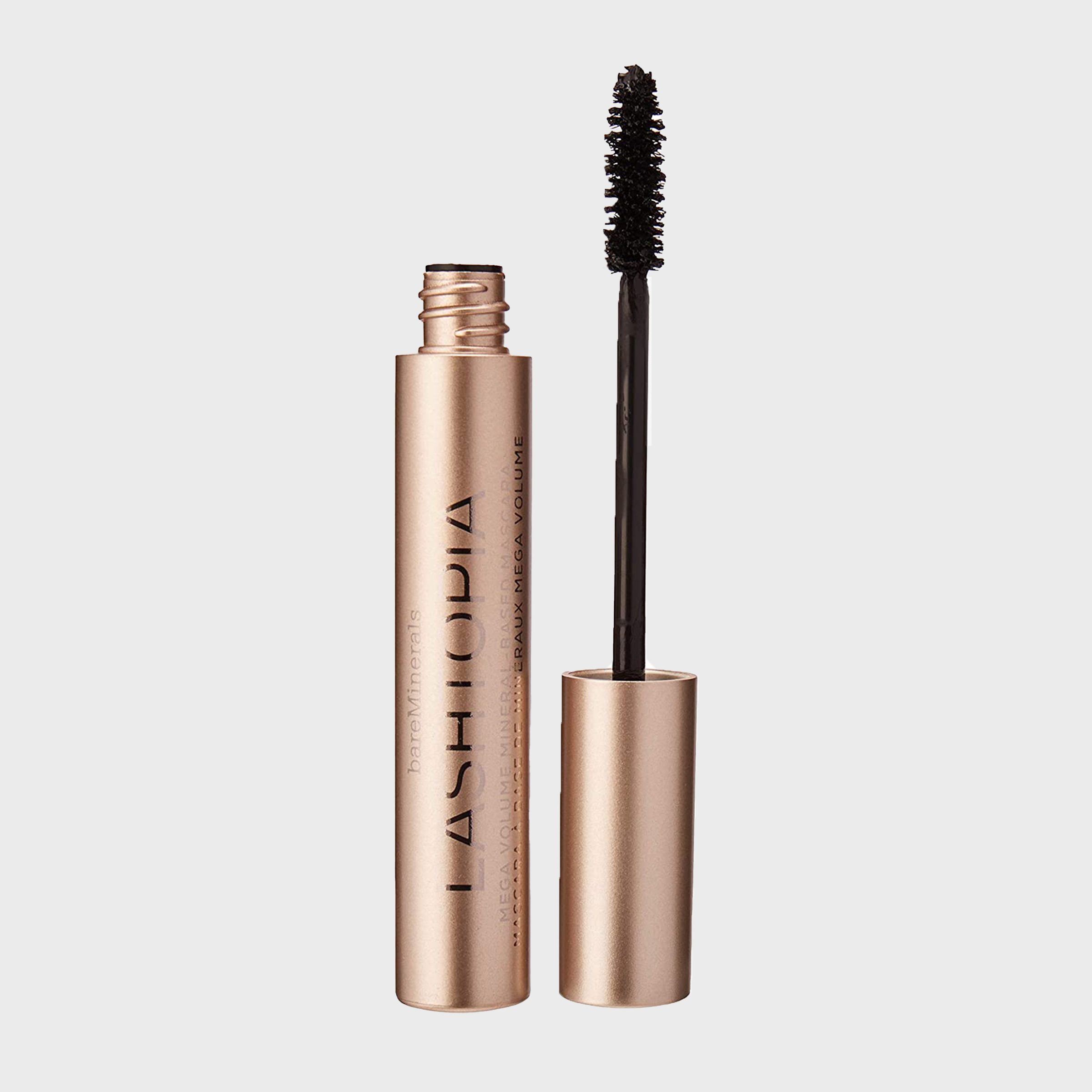 Mascara wand stands upright, removed from open gold tube labeled "LASHTOPIA" against a plain, white background.