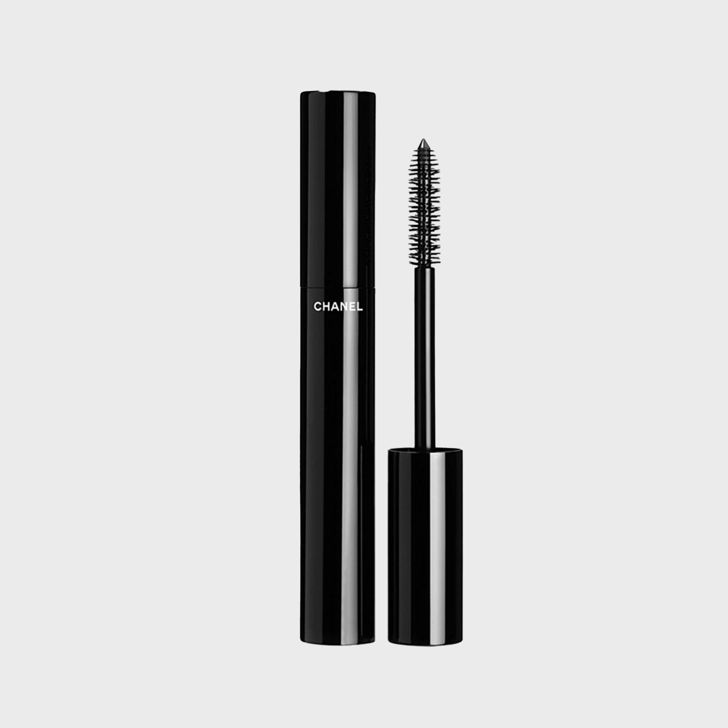 Mascara tube stands upright with an open applicator, featuring a black design and "Chanel" text, on a plain gray background.