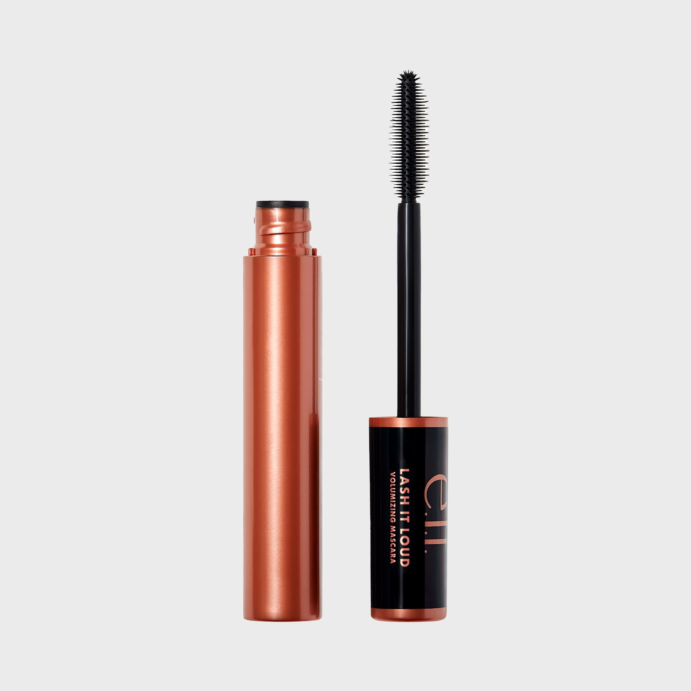 Mascara tube with bronze coloring stands open, revealing the black applicator wand. Text reads "e.l.f. Lash It Loud Volumizing Mascara." Plain gray background.