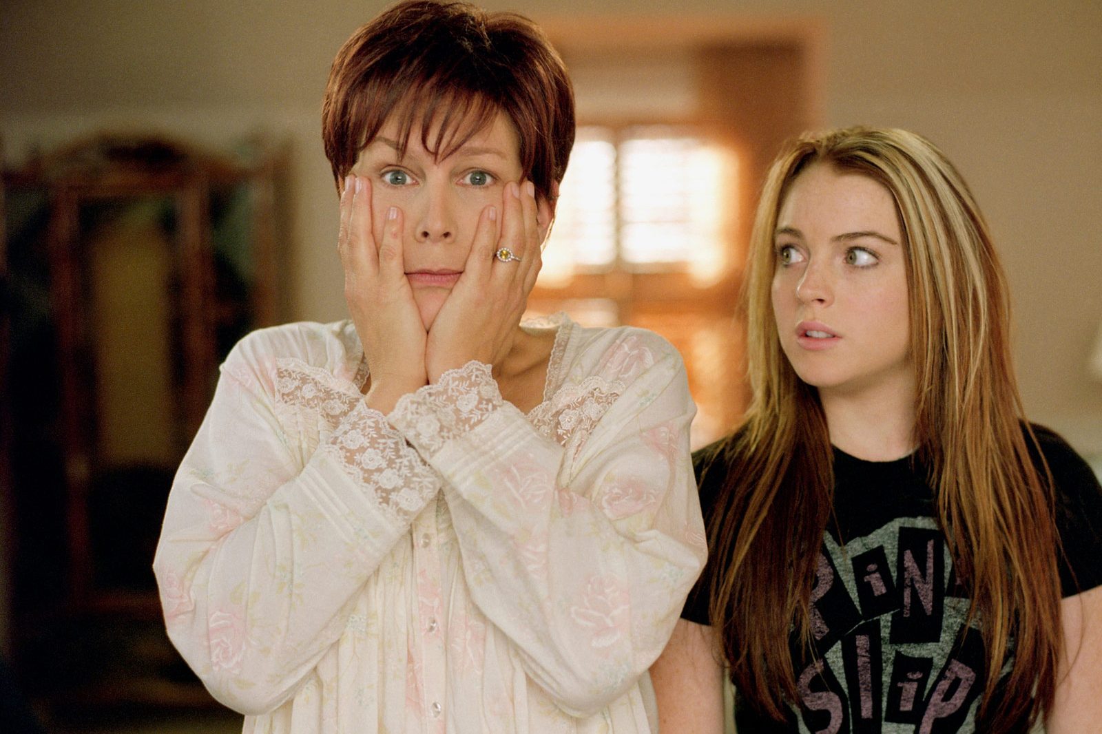 Two women stand indoors, one in pajamas with a shocked expression, hands on cheeks; the other looks at her, appearing surprised.