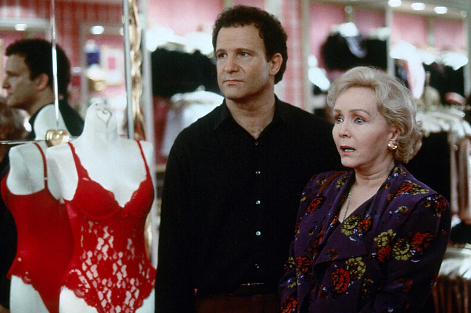 Mannequin displays red lingerie; a man and woman observe with mixed expressions in a brightly lit clothing store.