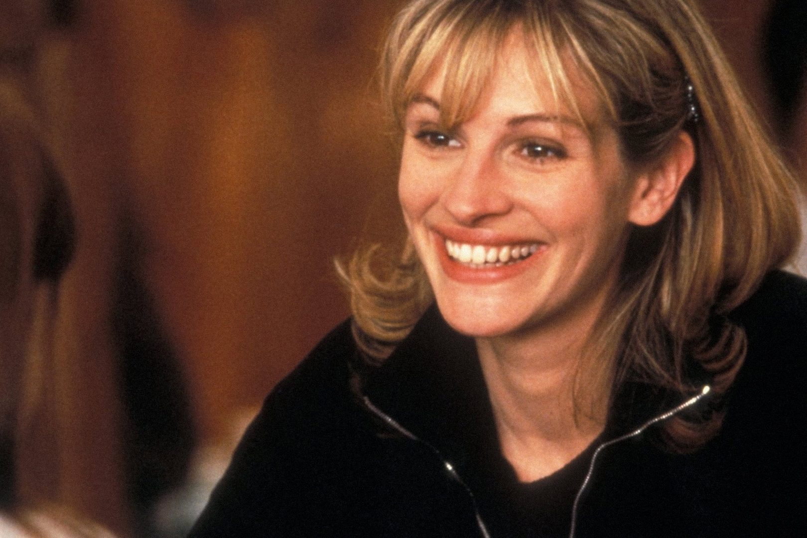 A person smiles broadly, looking engaged in conversation, set against a warm, softly focused background.