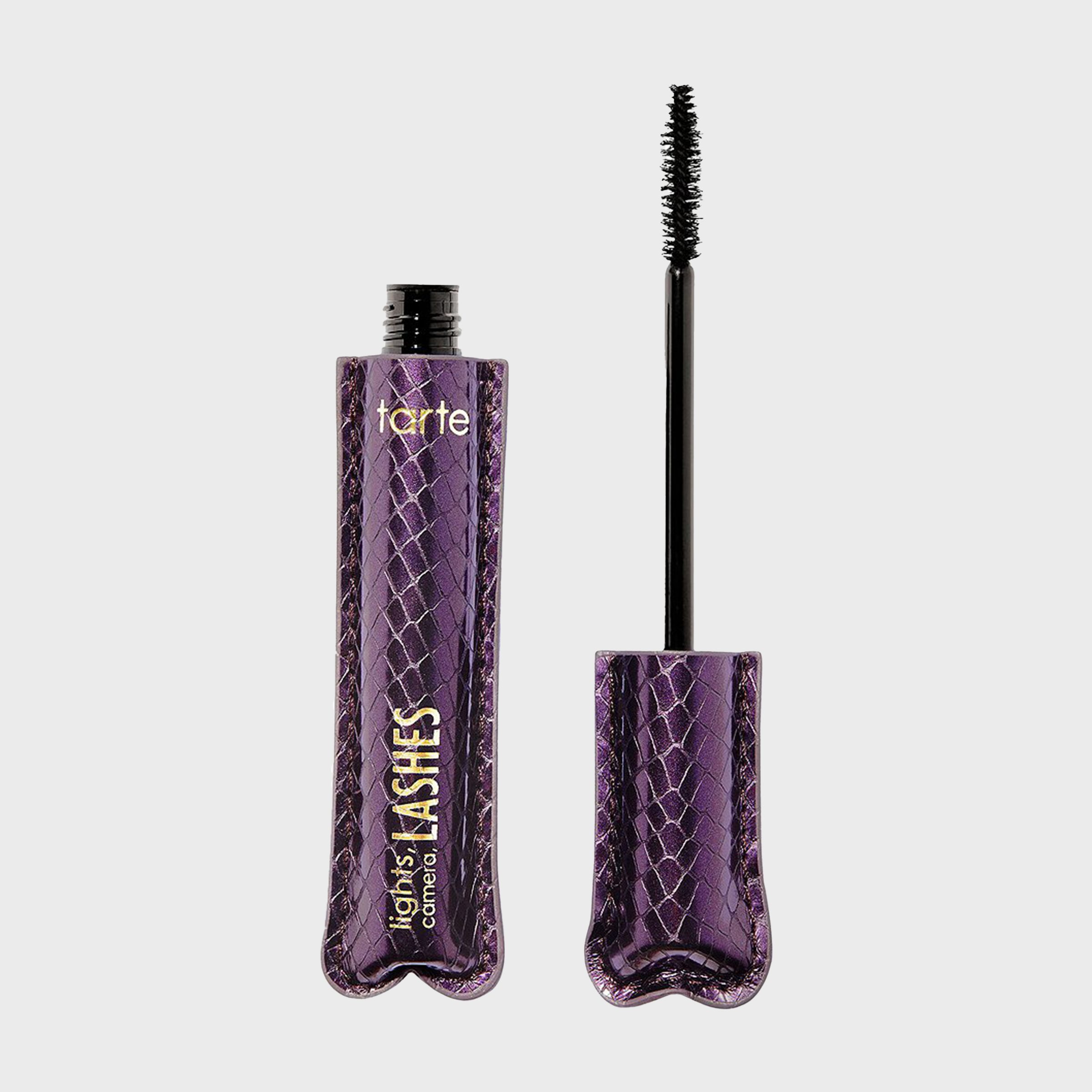 A mascara wand extends from a textured purple tube in a minimalistic setting.
