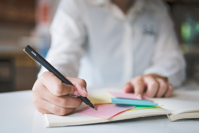 Close up and front view Cropped view of woman hand writing in notebook and sitting at table with laptop. Copy space concept