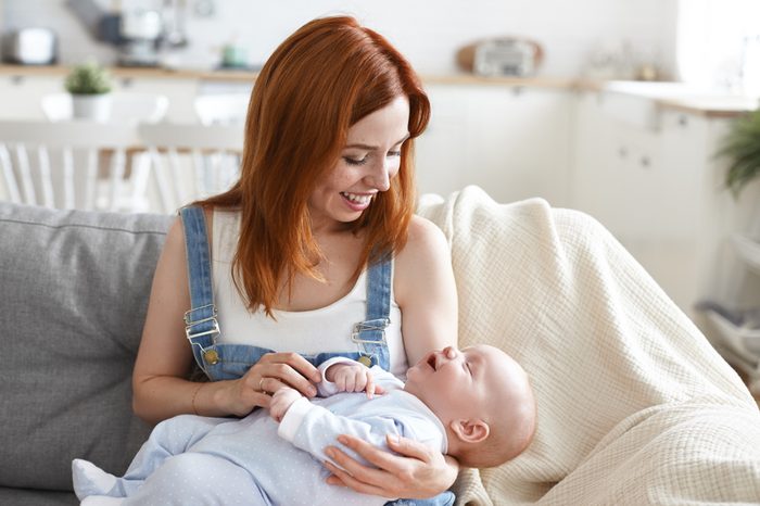Happy motherhood concept. Picture of cute joyful young European mom with ginger hair babysitting adorable infant at home, enjoying maternity leave, bonding with her baby, having cheerful smile
