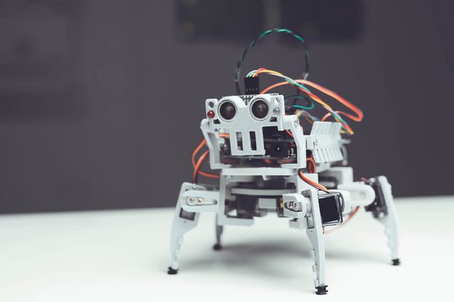 Robot close up. A small gray robot is on the table. Next to him an empty table and the background of the workshop in which he was created