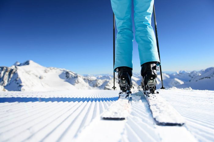 Girl on ski standing on the fresh snow on newly groomed ski piste at sunny day in mountains
