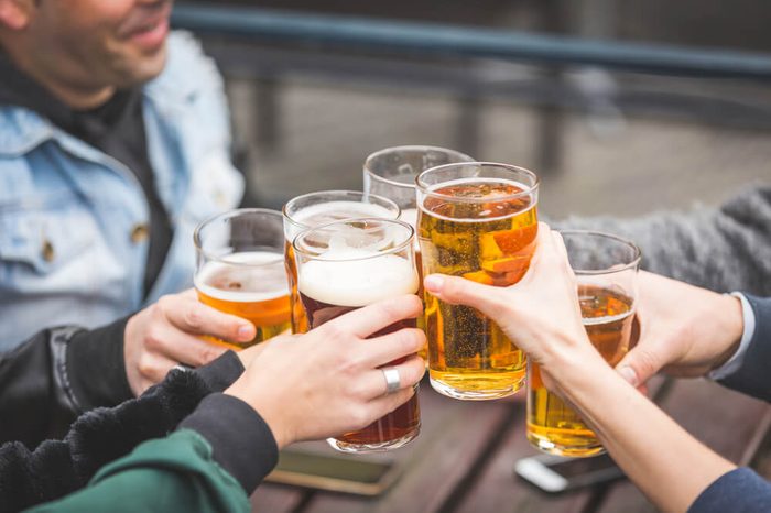 Group of friends enjoying a beer at pub in London, toasting and laughing. They are four girls and two boys in their twenties. Close up and focus on glasses.