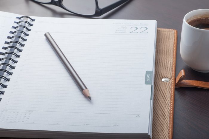 Close up of a working desk with a notebook, pencil, coffee cup and eyeglasses