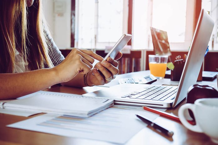 Close up of a woman hand using a smart phone with laptop on a desk at office