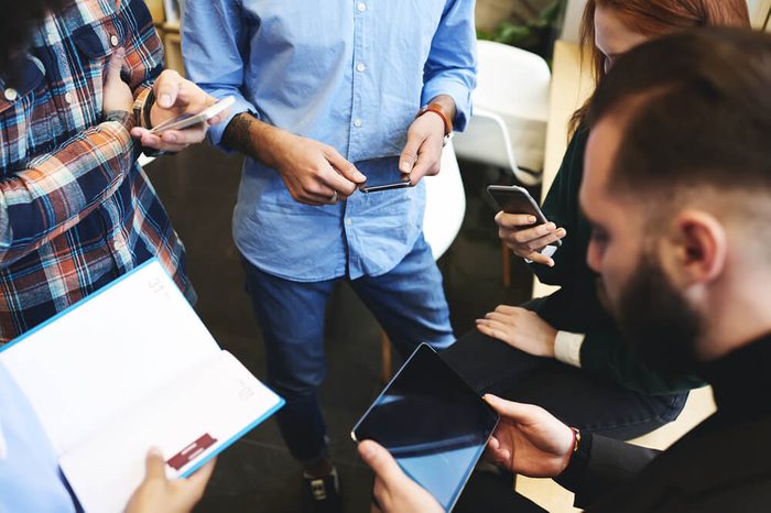 Team of male and female IT developers using digital gadgets with mock up screen and wireless connection to install new software for modern devices downloading apps from web page standing in office