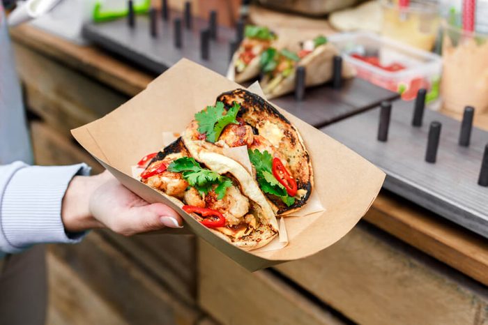 Female street vendor hands show fresh roasted meat and vegetables taco outdoors. Mexican cuisine snacks, fast food of commercial kitchen.
