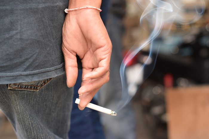 Image of cigarette in man hand with smoke.