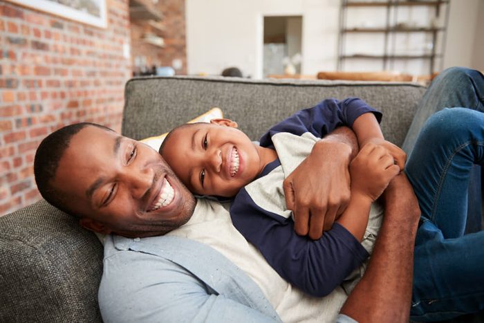 Father And Son Cuddling On Sofa Together
