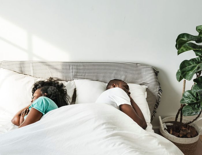 Black couple sleeping together on bed back to back
