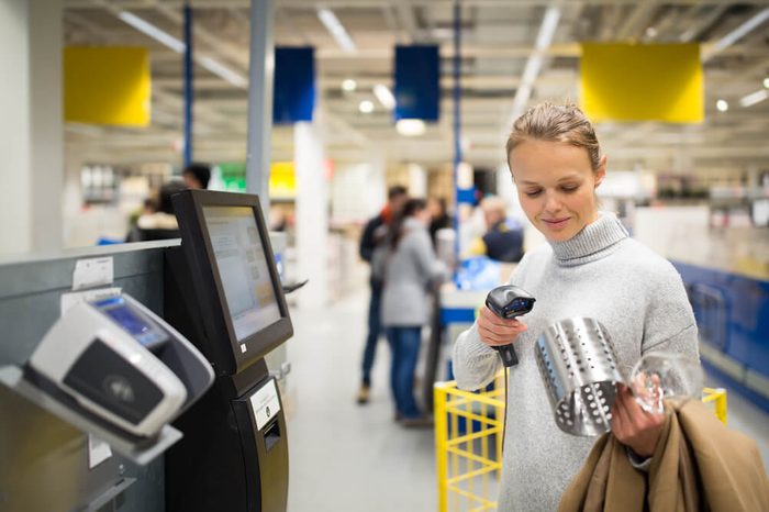Pretty, young woman using self service checkout in a store (shallow DOF; color toned image)