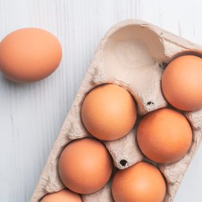 Carton contains five brown eggs; one egg rests separately on a light wooden surface.