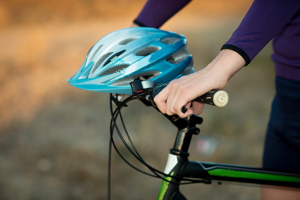 anonymous woman walking with her bike and the helmet is on the handlebars