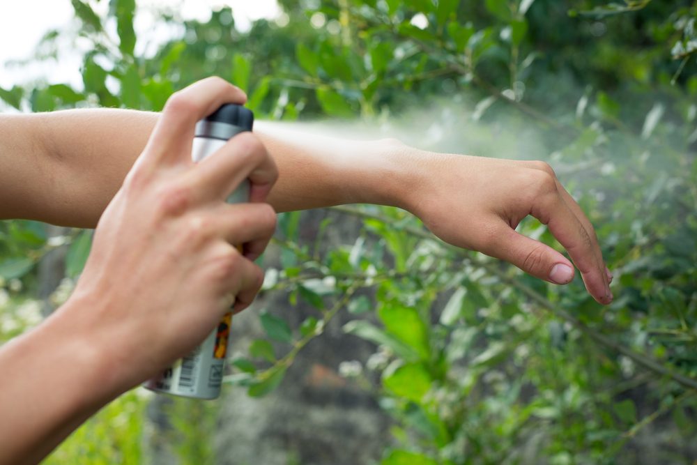 Young man spraying mosquito / insect repellent in the forrest, insect protection