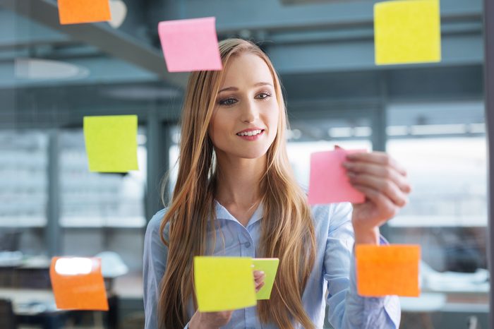Business plan. Young female professional sticking colourful notes to a glass wall