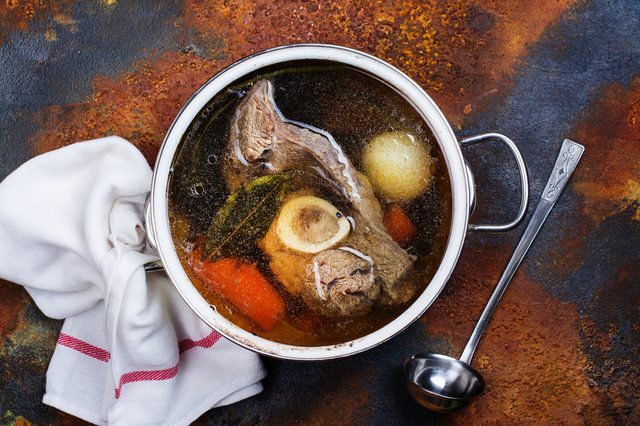 Broth soup in a cooking pot with ladle on dark stone background. Top view