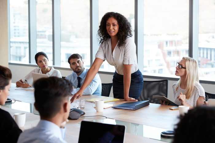 Businesswoman Stands To Address Meeting Around Board Table