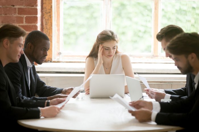 Serious multiracial businessmen holding documents at meeting with businesswoman, male diverse entrepreneurs considering new contract with female partner, employees reading woman boss instructions