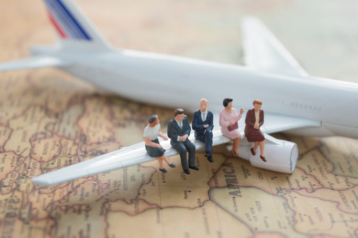 Miniature people : business team sitting on airplane wing for travel around the world, using as business trip traveler adviser agency or explorer on earth background concept.