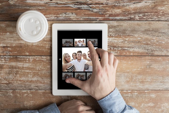 people, memory and technology concept - close up of male hands with picture of happy friends on tablet pc computer screen and coffee cup at table