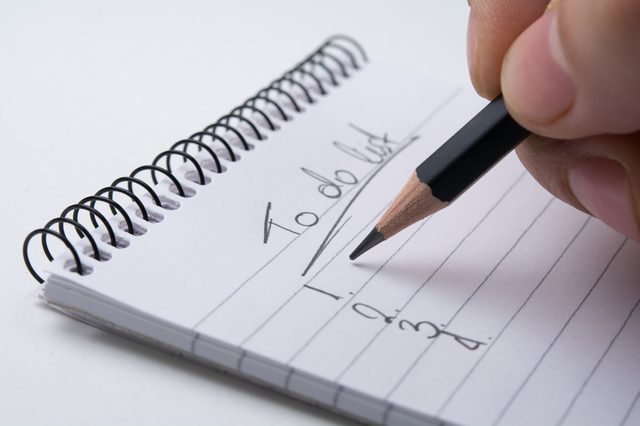 Close up of hand holding a pencil and writes the to do list. Isolated on white