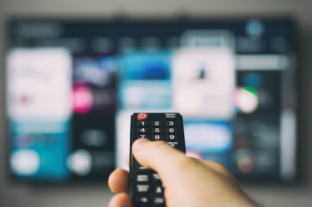 Male hand holding TV remote control.