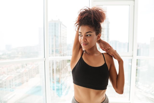 Image of african woman stretching hands before training yoga and looking aside at home