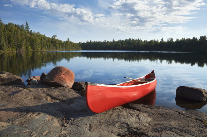 A red canoe rests on a rocky shore of a calm blue lake in the Boundary Waters of Minnesota