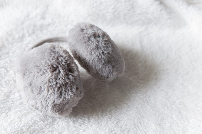 Winter accessories of Gray fur ear-muffs on white fur background, warm clothing for autumn or winter