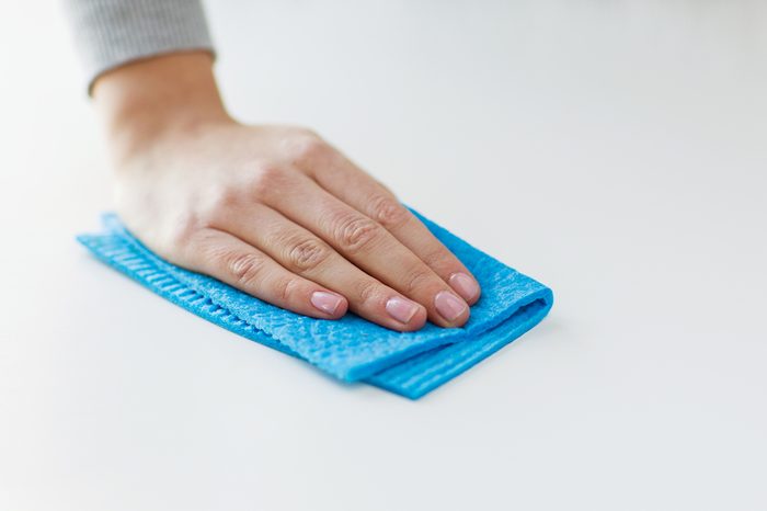 people, housework and housekeeping concept - close up of woman hand cleaning table surface with cloth at home
