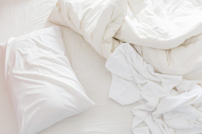 Top view of an unmade bed after waking up in the morning with a white pillow, a blanket and a shower towel on the bed.