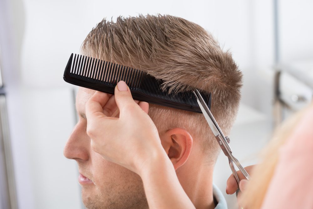 Young man getting haircut from female hairdresser at salon