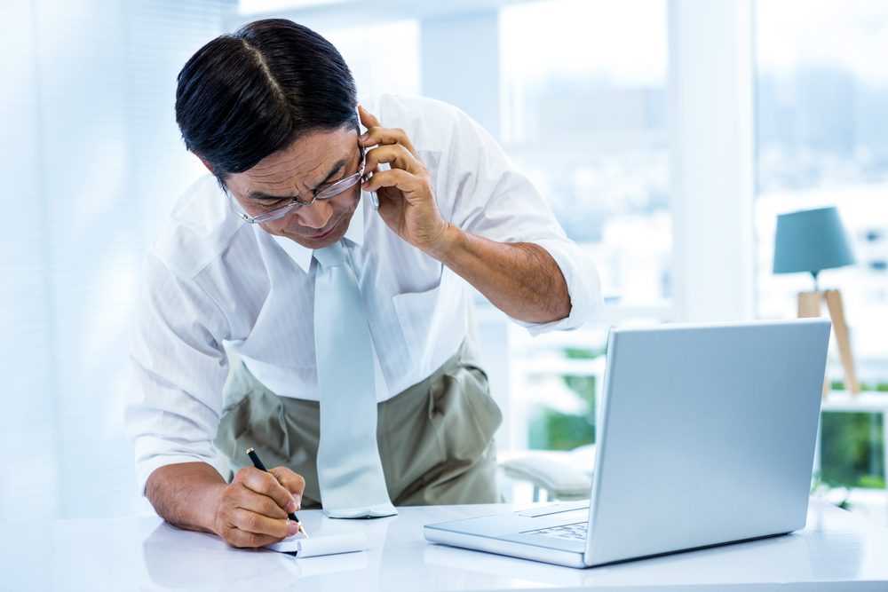 Overwhelmed asian businessman answering the phone and writing