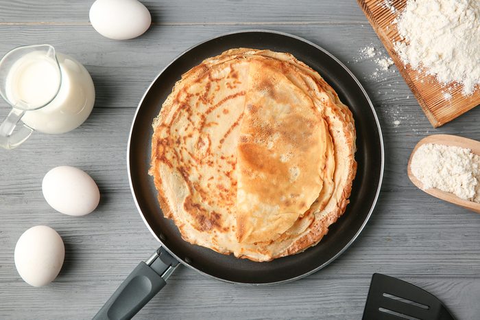Pan with delicious thin pancakes on wooden table